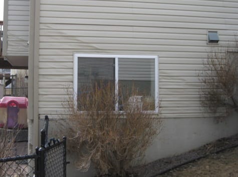 Siding repair by DFW Roofers in Plano, Texas, showing severe heat warping and bowing on beige vinyl siding panels under a window